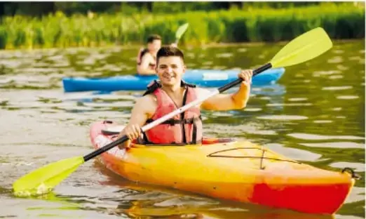 Persona remarando en un kayak amarillo sobre aguas tranquilas, con otra lancha azul al fondo.