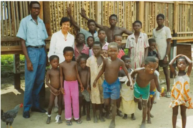 Fotografía de Evangelina Villegas Moreno junto a un grupo de niños y adultos en una comunidad rural, probablemente en un país africano, ilustrando su labor por combatir la desnutrición.