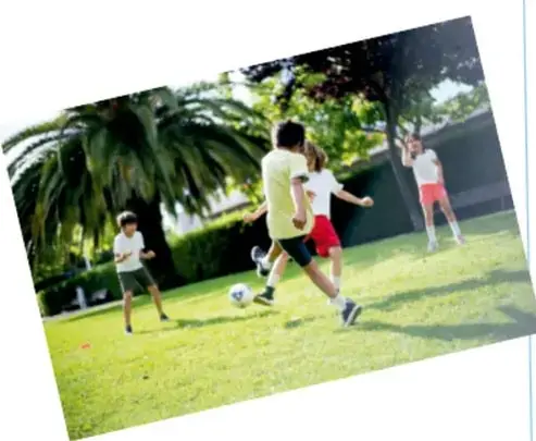 Fotografía de niños jugando fútbol en un parque con palmeras y césped, relacionada con la convivencia y el juego en equipo.