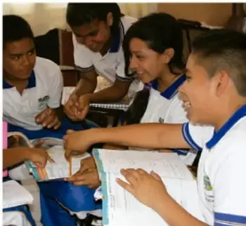 Fotografía de cuatro estudiantes de telesecundaria trabajando juntos alrededor de una mesa con cuadernos y materiales escolares.