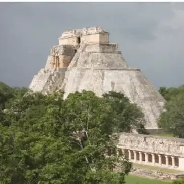 Fotografía de una pirámide y edificaciones de una ciudad maya clásica entre vegetación.