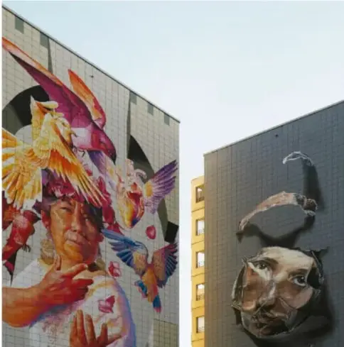 Fotografía de dos murales urbanos en fachadas: uno con el rostro de una mujer y aves multicolores (colibríes y guacamayas) alrededor; el otro con rostros con rocas pintadas sobre fachada de vidrio oscuro.