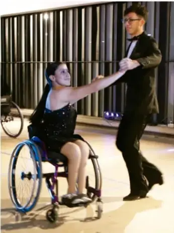 Pareja bailando: una mujer en silla de ruedas y un hombre de pie, representando inclusión, diversidad y actividad física empática.