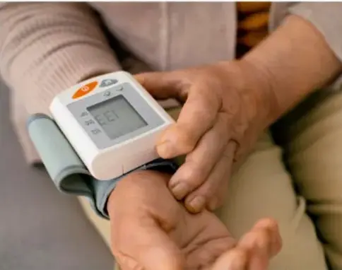 Mano de una persona con un baumanómetro digital colocado en la muñeca, midiendo la presión arterial.