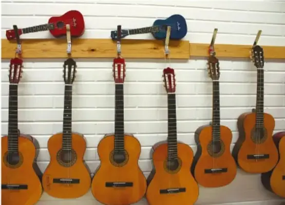 Fotografía de varias guitarras acústicas y un ukelele colgados en una pared blanca con listones de madera, como ejemplo de instrumentos elaborados o reunidos para un proyecto.