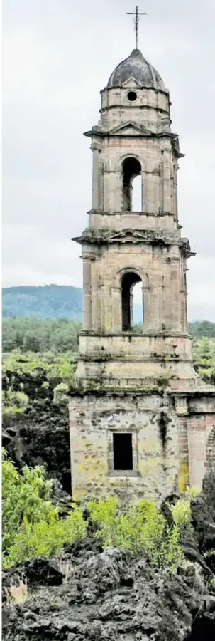 Fotografía de la torre de cantera de la iglesia de San Francisco Javier de Batuc, con arcos de campanario desgastados, entre vegetación y cerros.