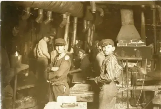 Fotografía en blanco y negro de trabajadores en una fábrica del siglo XIX, con maquinaria y vestimenta de la época.