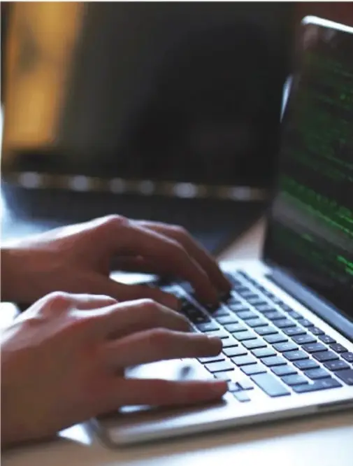 Manos escribiendo en el teclado de una laptop con código en la pantalla.