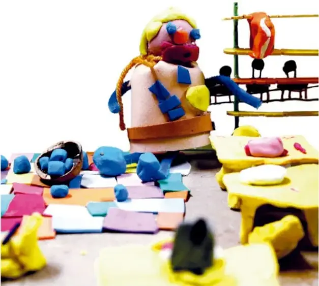 Fotografía de un escenario con personajes de plastilina, tapas de colores, cartulinas y materiales para stop motion.