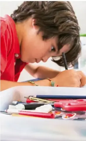 Fotografía de un estudiante dibujando con lápiz sobre papel, con colores y reglas sobre la mesa.