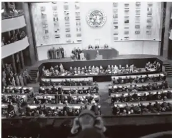 Fotografía en blanco y negro de una asamblea o recinto legislativo con muchas personas sentadas.