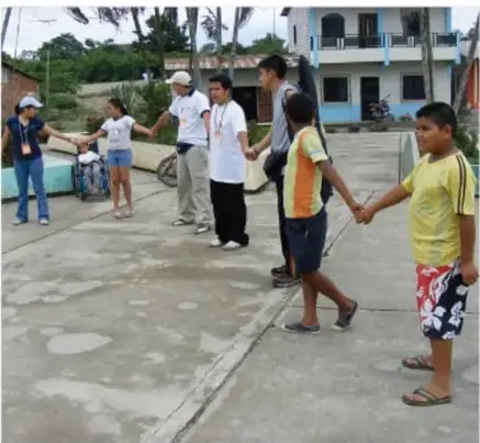 Niños y niñas tomados de las manos formando un círculo en el patio, acompañados por una persona adulta.