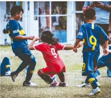 Fotografía de niños y niñas jugando fútbol en una cancha escolar; uno de ellos viste playera roja con el número 9.