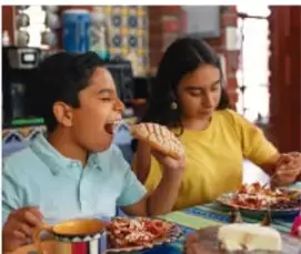 Dos niños comiendo en la mesa, ilustra cantidad de alimentos.