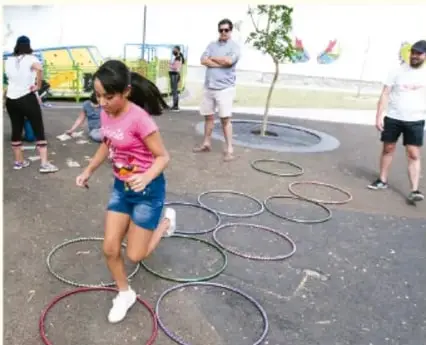 Fotografía de estudiantes saltando entre aros en una cancha al aire libre, con adultos observando.