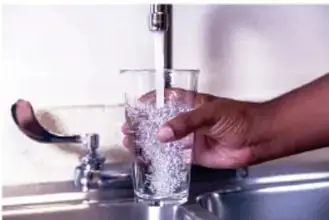 Manos llenando un vaso con agua de una llave.