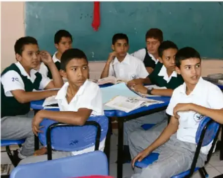Fotografía de estudiantes de secundaria en un aula, sentados en escritorios con uniformes blancos y verdes, participando en clase; ilustra un intercambio de opiniones en el ámbito escolar.