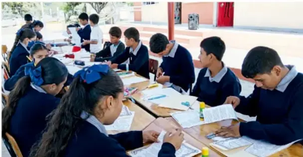 Foto de estudiantes de telesecundaria trabajando en comunidad alrededor de mesas.