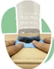 Manos sujetando con plastilina una botella en el orificio de una caja.