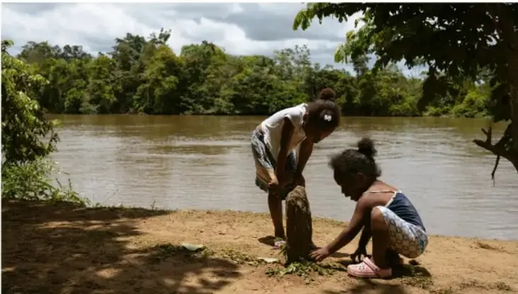 Fotografía de dos niñas junto a un río en un entorno natural con vegetación, probablemente en una comunidad afromexicana o indígena.