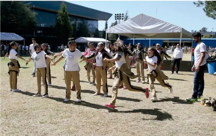 Fotografía de un grupo de estudiantes en uniforme participando en una actividad motriz al aire libre en una cancha, acompañados por un adulto que parece ser el docente; se observa movimiento, interacción y dinamismo en el juego.
