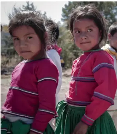 Fotografía de dos niñas con cabello largo, con blusas rosas y faldas verdes, de pie al aire libre, que ilustra la diversidad cultural de las comunidades escolares.