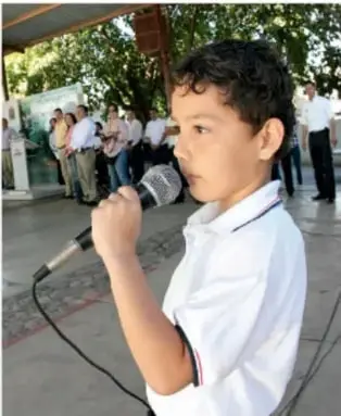 Niño hablando por micrófono durante una presentación escolar al aire libre.