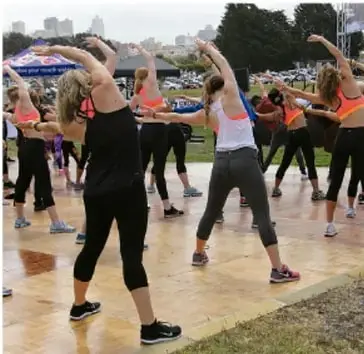 Foto de un grupo de mujeres en un parque realizando ejercicios de estiramiento lateral con los brazos elevados.