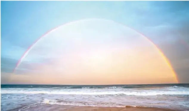Fotografía de un arcoíris sobre el mar al atardecer, ilustrando fenómenos ópticos naturales.