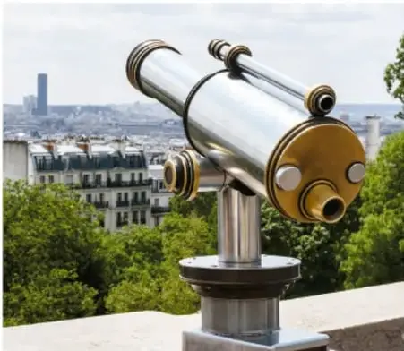 Fotografía de un telescopio óptico montado sobre una base, con una ciudad al fondo.