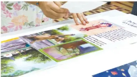 Fotografía de manos manipulando materiales de un libro álbum narrativo con imágenes y textos sobre una mesa, en el proceso de lectura, análisis o intercambio de materiales.