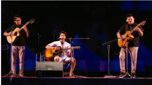 Fotografía de tres músicos en escenario nocturno tocando guitarras, iluminados con luz azul de fondo.