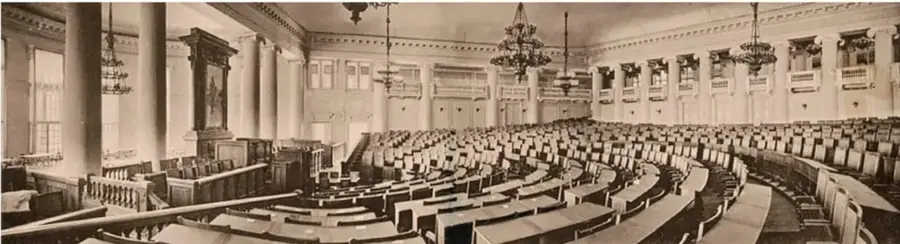 Fotografía en blanco y negro del interior de la Duma Imperial de Rusia, con bancas curvas, columnas y lámparas de araña.