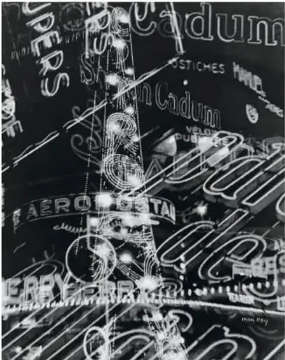 Fotografía en blanco y negro de letreros luminosos y anuncios urbanos, con la firma 'Man Ray' en la esquina inferior derecha.