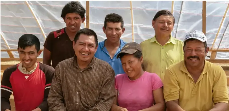 Fotografía de un grupo de siete personas (seis hombres y una mujer) sonriendo frente a la cámara, integrantes de una cooperativa, dentro de lo que parece ser un invernadero o estructura agrícola con lámina translúcida.