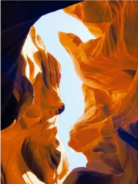 Fotografía a color del Cañón del Antílope en Arizona: paredes de roca onduladas en tonos naranja y marrón con cielo azul al fondo.