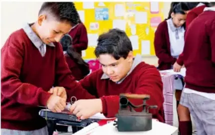 Estudiantes trabajando con equipo tecnológico (posiblemente una réplica o dispositivo) en equipo, colaborando en la elaboración del producto.