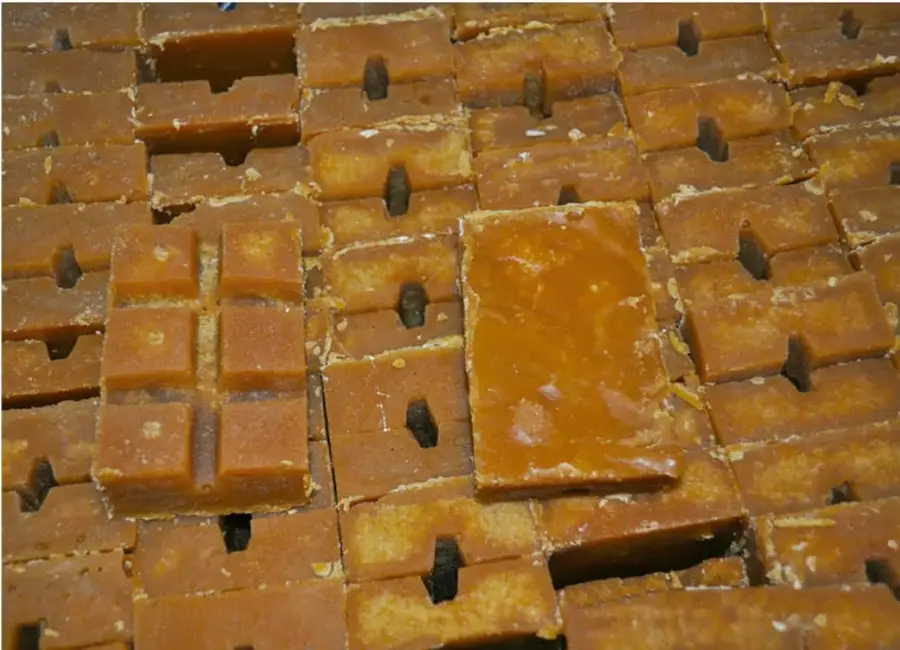 Fotografía de múltiples paquetes rectangulares de panela artesanal de color café oscuro, con orificios en el centro, apilados en filas. Algunos presentan marcas en forma de cruz grabadas en la superficie.