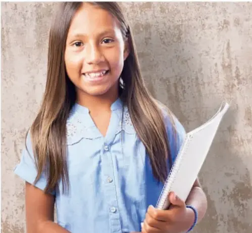 Fotografía de una niña sonriente sosteniendo un cuaderno, con uniforme escolar.