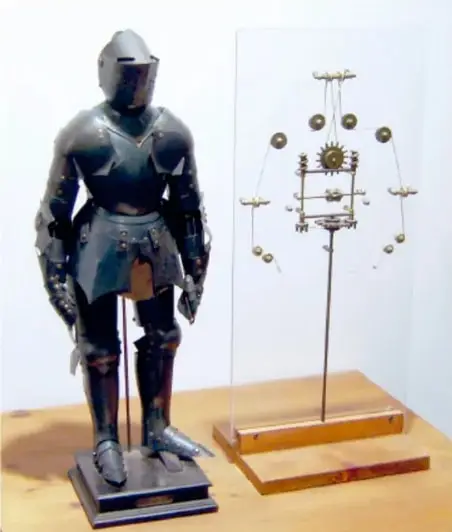 Fotografía de una réplica del Automa cavaliere: armadura metálica de caballero de pie sobre una base, junto a un esquema mecánico con engranajes y poleas que muestra su funcionamiento interno.