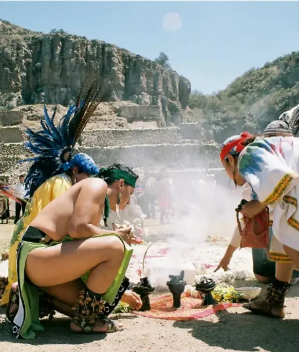 Ceremonia de una cultura originaria: mujeres y hombres con atuendos tradicionales realizan un ritual con humo, flores y ofrendas en un espacio al aire libre.