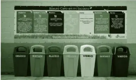 Fotografía en tono verde de una fila de contenedores de separación de residuos con rótulos visibles como ORGÁNICO, BOTELLAS, PLÁSTICO, VIDRIO y VARIOS (algunos rótulos poco legibles), bajo un cartel de reciclaje.