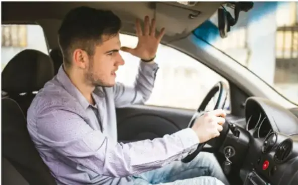 Fotografía de un hombre joven conduciendo un automóvil con una mano en el volante y la otra cerca de la ventanilla, ilustra conductas viales y autocuidado en el transporte.