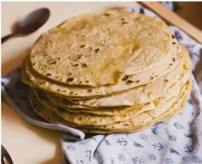 Fotografía de un plato con tortillas de maíz apiladas sobre una tela bordada, con una cuchara de madera al lado.