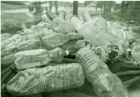 Fotografía en tono verde de un montón de residuos plásticos: botellas PET vacías y envases aplastados.