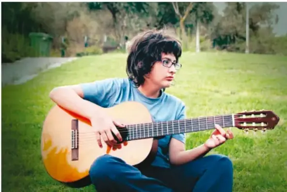 Adolescente sentado en el pasto de un parque tocando una guitarra acústica, representando el ejemplo del joven músico.