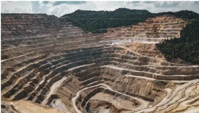Fotografía de una mina a cielo abierto con terrazas escalonadas excavadas en la roca, rodeada de vegetación.