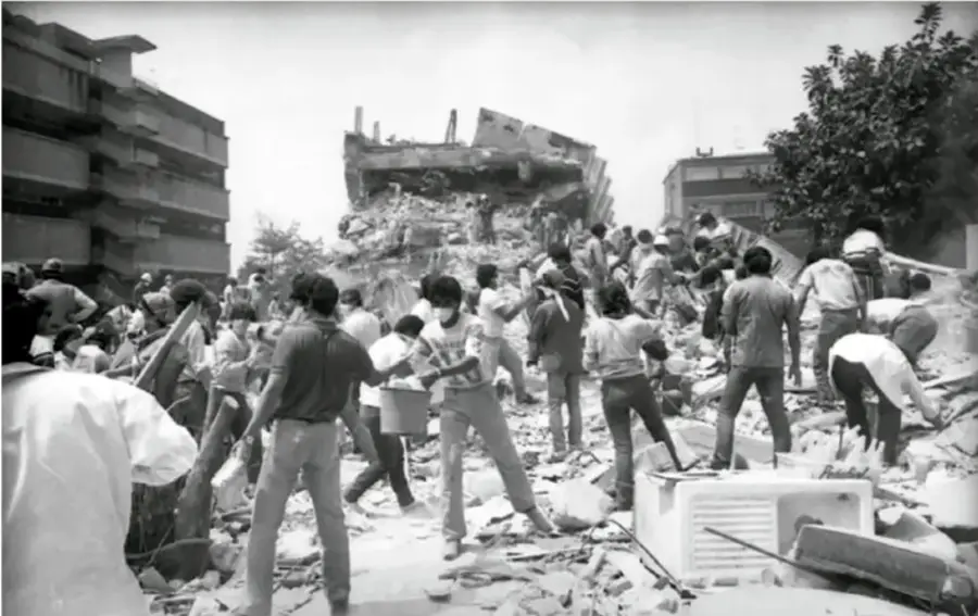 Fotografía en blanco y negro del sismo de 1985 en México: civiles y rescatistas trabajando entre escombros de edificios colapsados, cargando materiales y buscando supervivientes.