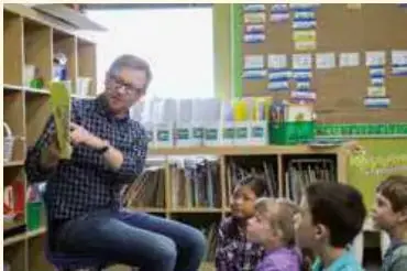Profesor leyendo un libro a un grupo de estudiantes en la biblioteca.