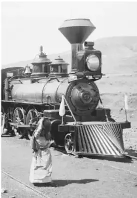 Fotografía en blanco y negro de una locomotora de vapor con una persona caminando junto a ella, símbolo del progreso porfiriano.
